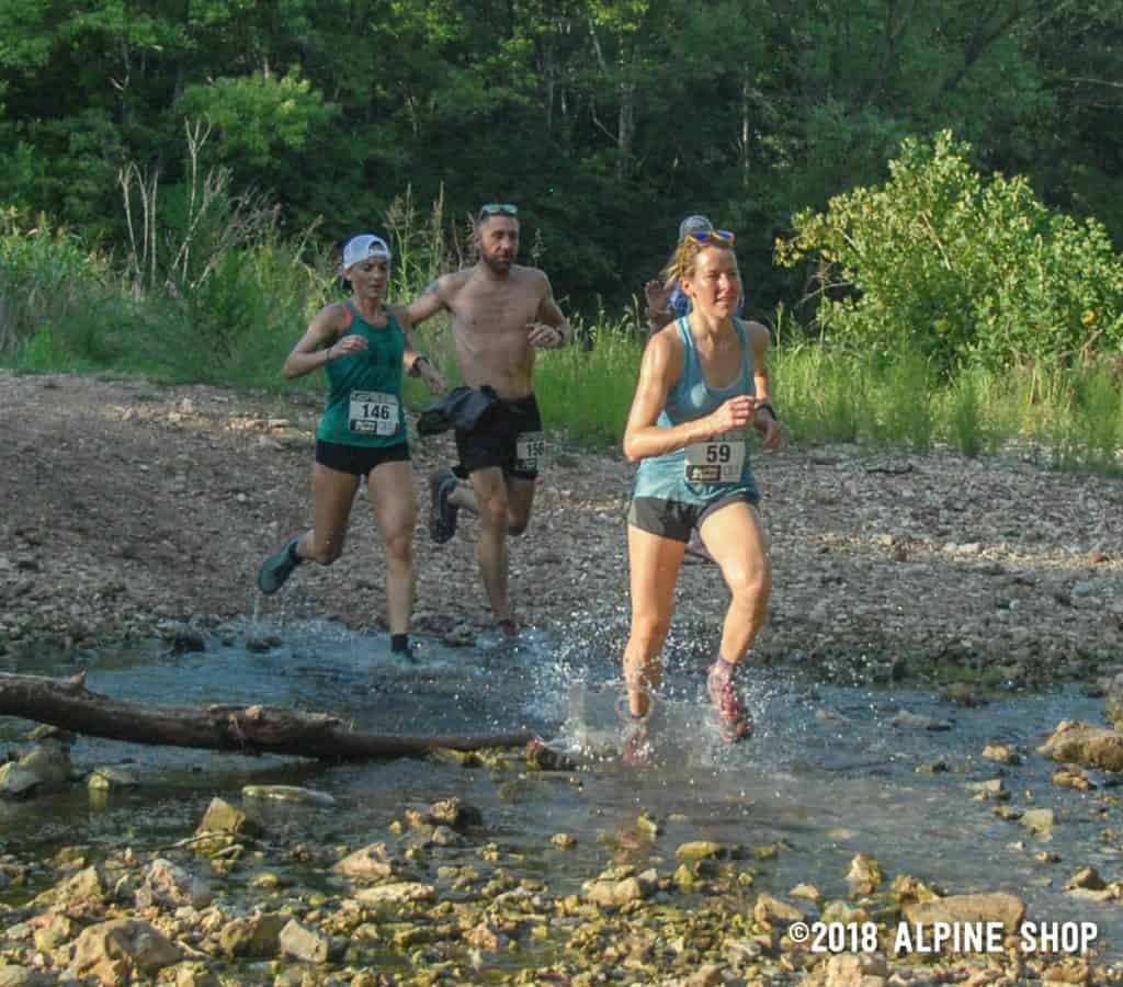 Women's division winner Hannah Floyd (at right, #59) closely pursued by second-place finisher Jaime Maher (#146), along with Dennis Martin (#156) at the creek crossing on the 4.1 mile course.